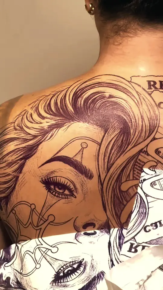 Decalque roxo de um rosto feminino aplicado nas costas, com o papel ainda saindo.